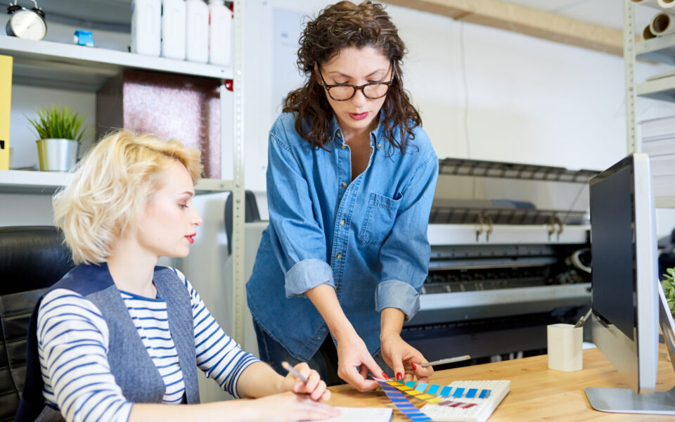 Graphic Designers in Printing Shop Portrait of two graphic designers choosing color palette from swatches while working at desk in printing shop or publishing company, copy space